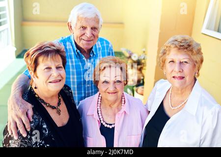 Zurück zu uns selbst zu sein. Aufnahme einer Gruppe fröhlicher älterer Menschen, die vor einem Gebäude lächeln und für die Kamera posieren. Stockfoto