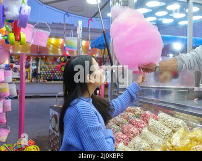 Frau, die während einer nächtlichen Messe eine Zuckerwatte von einem Händler kauft Stockfoto