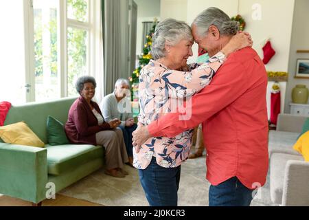 Glückliches kaukasisches Seniorenpaar, das zur weihnachtszeit vor ihren vielfältigen Freunden tanzt Stockfoto