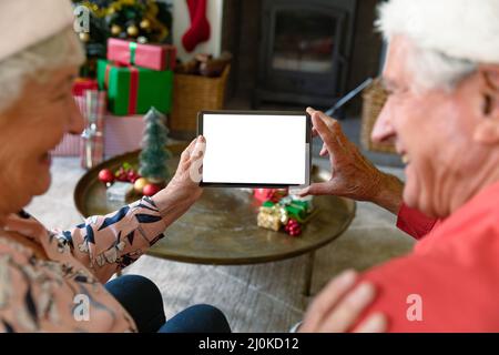 Kaukasisches Seniorenpaar trägt weihnachtsmützen und verwendet zur weihnachtszeit ein Tablet mit Platz zum Kopieren Stockfoto