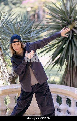 Die junge Frau im Hip-Hop-Stil steht in einer Pose im Park vor dem Hintergrund von Palmen Stockfoto