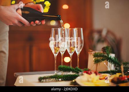 Gläser Champagner auf Holztisch mit Kerzen gegen verschwommene Wand mit weihnachtlicher Dekoration Stockfoto