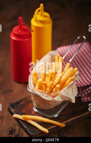 Pommes frites in einem Metallkorb auf einem Holzbrett. Fast-Food-Konzept, amerikanische Küche Stockfoto