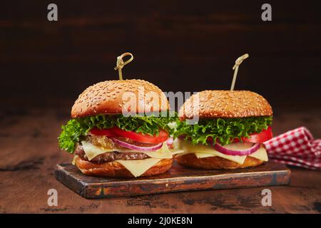 Zwei hausgemachte Burger mit Rind-, Käse- und Zwiebelmarmelade auf einem Holzbrett. Fast-Food-Konzept, amerikanische Küche Stockfoto