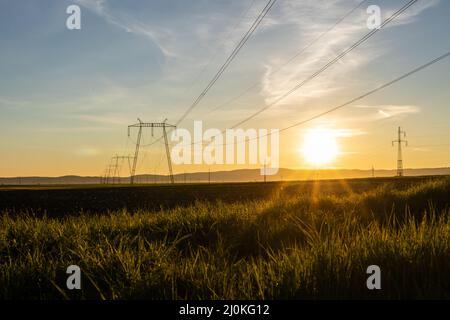 Hochspannungstürme und Hochspannungsleitungen bei Sonnenuntergang. Stockfoto