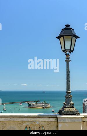 Alter Laternenpfosten an einer Wand mit Blick auf das Meer und die historische Festung in Salvador Stadt Stockfoto