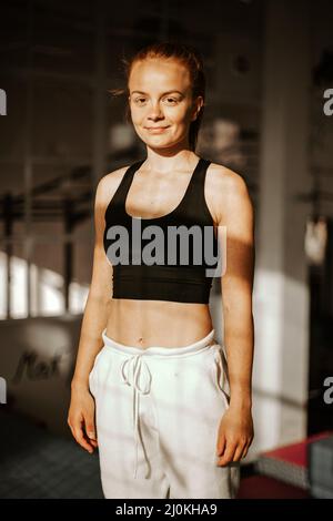 Hochformat . Junge attraktive lächelnde Frau Athlet in Sportkleidung in der Turnhalle . Sonnenuntergang Stockfoto