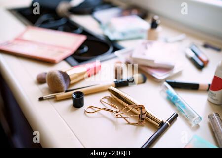 Make-up Artist Set. Nahaufnahme von Wimpern-Lockenwickler und Mascara in goldener Verpackung mit Make-up-Bürsten auf einem verschwommenen Fensterbrett Stockfoto