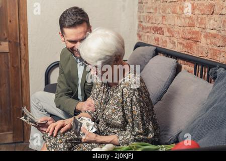 Die Mutter der europäischen Rentnerin lacht laut, während sie alte Fotos ansieht und mit ihrem Sohn mittleren Alters den Muttertag feiert. Hochwertige Fotos Stockfoto