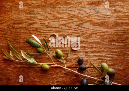 Goldene Eheringe und ein Verlobungsring auf braunem Hintergrund mit einem Zweig von Olivenbäumen. Stockfoto