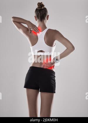 Ich muss das auschecken lassen. Schuss einer jungen Frau, die ihren verletzten Rücken und ihre verletzte Schulter in rot markiert hält. Stockfoto