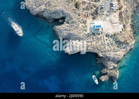 Drohnenaufnahme der Halbinsel Cape Greko mit der Agioi Anargyroi Kirche auf den Felsen. Kreuzfahrt touristische Boote segeln. Stockfoto