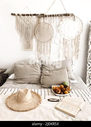 Romantisches schlafzimmer im scandi Boho-Stil mit Rattanhut, frischem Obst und offenem Buch auf dem Bett Stockfoto