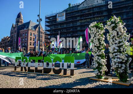 Während der Demonstration wurden mehrere weiße Blüten gesehen, die die Zahl elf repräsentieren. Im März 2011, nach vier Jahrzehnten Diktatur, erhob sich das syrische Volk friedlich, um Demokratie und würde zu fordern. Das Regime von Baschar al-Assad hat diesen Aufstand mit Gewalt niedergeschlagen und einen internationalen Krieg ausgelöst, der mehr als 500.000 Menschen getötet und 12 Millionen Menschen aus ihren Häusern vertrieben hat. Elf Jahre später versammelten sich Syrer in Amsterdam auf dem Dam-Platz, um weiterhin ihre legitimen Rechte, Freiheit und ein friedliches Syrien einzufordern. Stockfoto