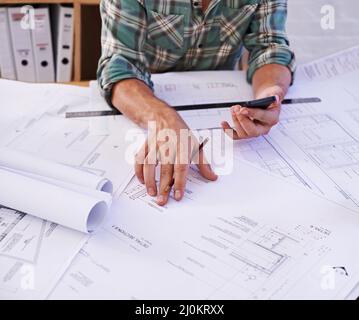 Design für Profis. Ausgeschnittene Aufnahme eines männlichen Architekten, der an einem Tisch an Blaupausen arbeitet. Stockfoto