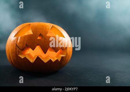 Komposition aus halloween geschnitztem Kürbis und Rauchwolke mit Kopierfläche auf blauem Hintergrund Stockfoto