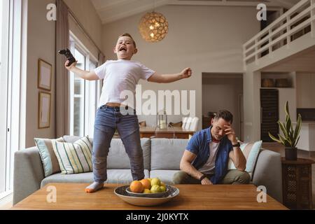 Kaukasischer Junge feiert auf dem Tisch stehen, während er Videospiele mit seinem Vater zu Hause spielt Stockfoto