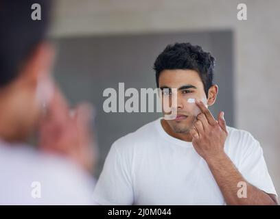 Das beste Hautpflegeprodukt für maximale Feuchtigkeit. Aufnahme eines hübschen jungen Mannes, der Feuchtigkeitscreme auf sein Gesicht anwendet. Stockfoto