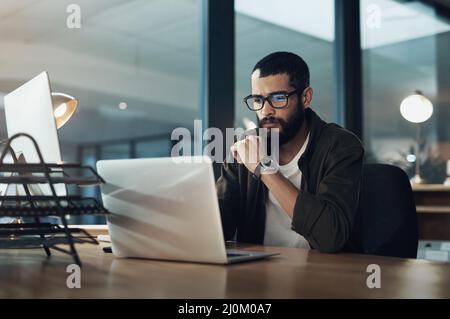 Je mehr Sie sich konzentrieren, desto schneller finden Sie die Lösung. Aufnahme eines jungen Geschäftsmannes, der einen Laptop während einer späten Nacht in einem modernen Büro benutzt. Stockfoto