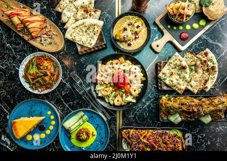 Indische Gerichte mit Pfeffer, Korma, Karottenkuchen, gefüllten Samosas, Knoblauchbrot, Naan, Vindaloo, Tikka Masala, Palak Paneer und Onion Bhaji Stockfoto