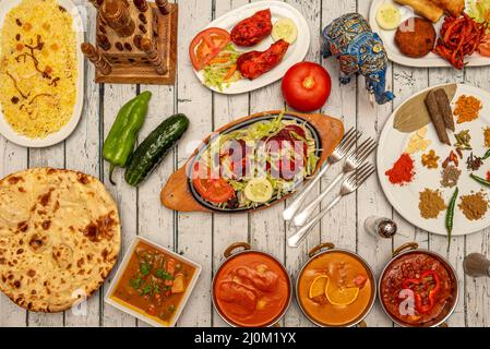 Typische indische Gerichte mit vielen Currys, mild und stark, Naan, Pilau-Reis, Tandoori-Huhn, Paprika und Gurken sowie verschiedene Gewürze Stockfoto