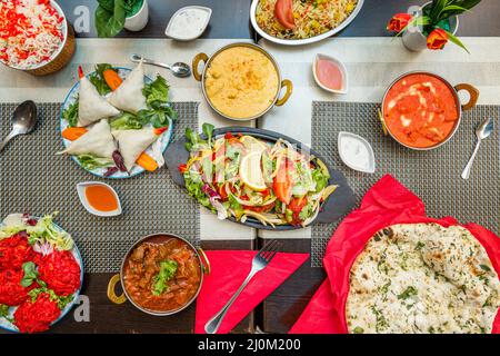 Traditionelle indische Küche mit rotem, gelbem Korma, Kokosnuss, Gabeln, Tandoori-Hähnchenplatte mit Gemüse, roten Zwiebeln Bhaji, Fleisch und Gemüsesa Stockfoto