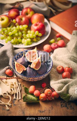 Gericht mit Feigen, Äpfeln und Trauben mit warmen, gemütlichen Strickwaren, Herbstblättern und Äpfeln. Stockfoto