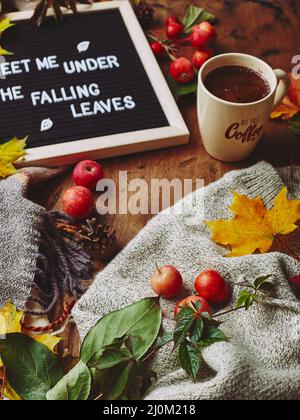 Herbst-Flatlay mit Briefbrett, kuscheligem Pullover und Schal, Tasse Kaffee, bunten Blättern und kleinen Äpfeln auf Holzhintergrund Stockfoto