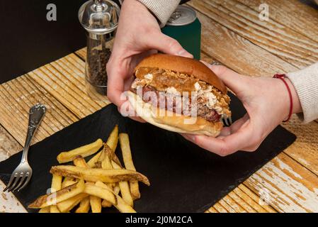 In zwei Händen einen Rinderburger mit Frischkäse, knusprigen und karamellisierten Zwiebeln halten Stockfoto