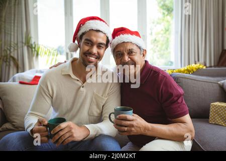 Porträt eines glücklichen erwachsenen Sohnes und älteren Vaters aus Birazialen in Weihnachtsmützen, der einen Weihnachtsvideoanruf führt Stockfoto