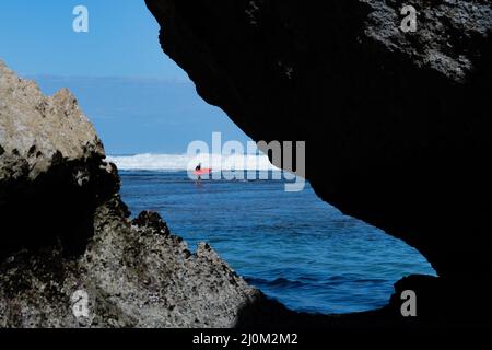 Ein Mann, der auf dem roten Surfbrett im Meer schwimmt. Stockfoto