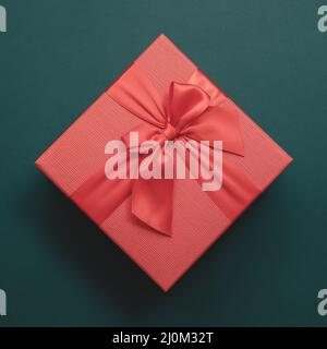 Rote Box mit Schleife auf smaragdfarbenem Hintergrund. Draufsicht. Anwesend Stockfoto