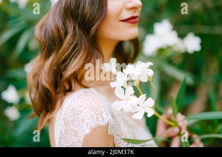 Die Braut steht bei einem blühenden weißen Oleander und hält einen Oleander-Zweig in der Hand, Nahaufnahme Stockfoto
