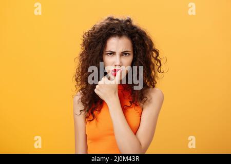 Waist-up Schuss von ernst entschlossen und konzentriert unzufrieden Frau mit lockigen Frisur runzelte bissing Daumen sieht gefährlich und Stockfoto