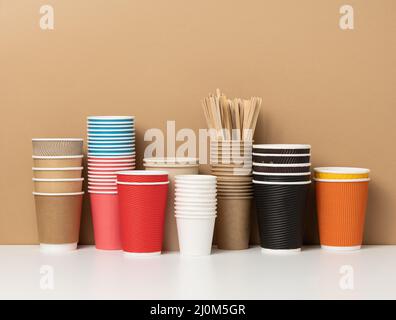 Stapel von verschiedenen Einweg-Pappbechern für Getränke, Kaffee und Tee auf einem weißen Tisch. Getränkebehälter zum Mitnehmen Stockfoto