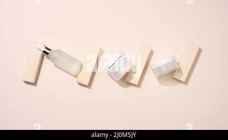 Kunststoffbecher und weiße Glasflasche mit Pipettenständer auf beigem Hintergrund. Kosmetik-SPA-Branding. Verpackung für Gel, Serum, Stockfoto