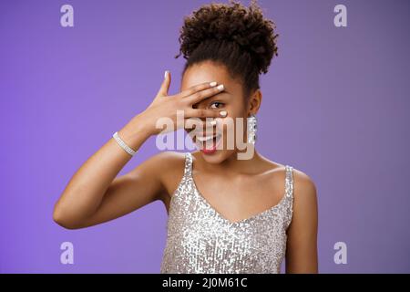 Close-up stilvolle afroamerikanische Frau Afro Frisur brillante Accessoires glitzernden silbernen Kleid versteckt Gesicht spähen durch Stockfoto