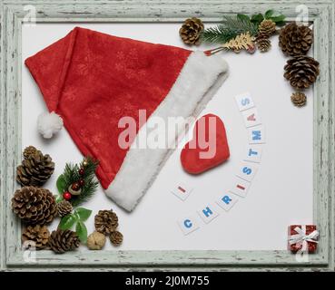 Rote Mütze und Herz in einem Rahmen mit einer weihnachtlichen Inschrift und Utensilien. Weihnachtskarte. Layout-Komposition Stockfoto
