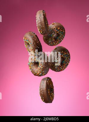 Schokolade runde Donuts mit bunten Zuckerstreuseln schweben auf einem rosa Hintergrund Stockfoto