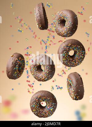 Runde Schokoladendonuts mit bunten Zuckerstreuseln schweben auf beigem Hintergrund Stockfoto