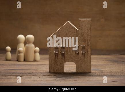 Hölzerne Familienfiguren, Modellhaus auf braunem Hintergrund. Immobilienkauf, Mietkonzept Stockfoto