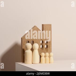 Hölzerne Familienfiguren, Modellhaus auf beigefarbenem Hintergrund. Immobilienkauf, Mietkonzept. Umzug in neue Wohnungen Stockfoto