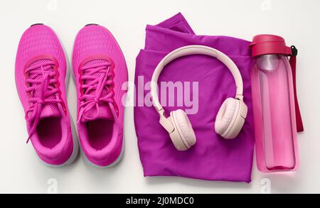 Ein Paar lila Textil-Sportschuhe, kabellose Kopfhörer, ein Handtuch und eine Flasche Wasser auf weißem Hintergrund. Sportbekleidung Stockfoto