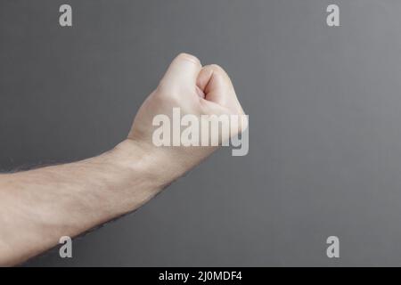 Männliche Hand, die eine Faust auf einem hellgrauen Hintergrund zusammenhält, Nahaufnahme. Speicherplatz kopieren. Stockfoto