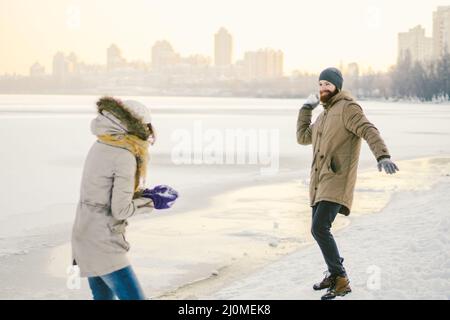 Junge kaukasische Menschen, die sich in heterosexuellen Paaren verliebt haben, haben im Winter ein Datum in der Nähe eines gefrorenen Sees. Aktivurlaub Valentinstag Stockfoto