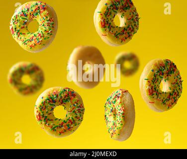 Runde gebackene Donuts mit vielfarbigem Zucker bestreut schweben auf einem gelben Hintergrund Stockfoto