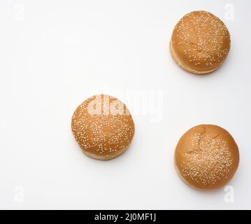 Gebackenes rundes, frisches Weizenmehl-Brötchen, bestreut mit Sesamsamen auf einem weißen Tisch. Hamburger, Cheeseberger und Sandwich-Brötchen Stockfoto