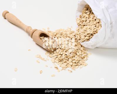 Roher Haferbrei in einem weißen Papierbeutel und ein Holzlöffel auf einem weißen Tisch, Frühstücksbrei Stockfoto