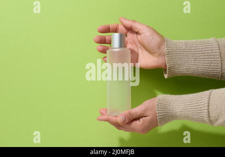 Weibliche Hand hält leere Plastikbehälter für flüssige Produkte, Seife oder Shampoo auf grünem Hintergrund Stockfoto