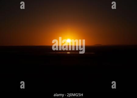 Makelloser goldener Sonnenuntergang über dem Ackerland, der sich im Wasser mit Bergen im Hintergrund widerspiegelt Stockfoto